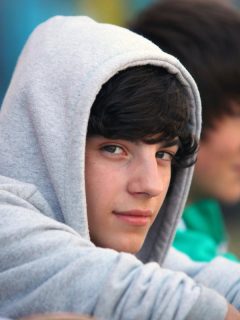 3 teens outdoors, boy in gray hoodie looking at camera