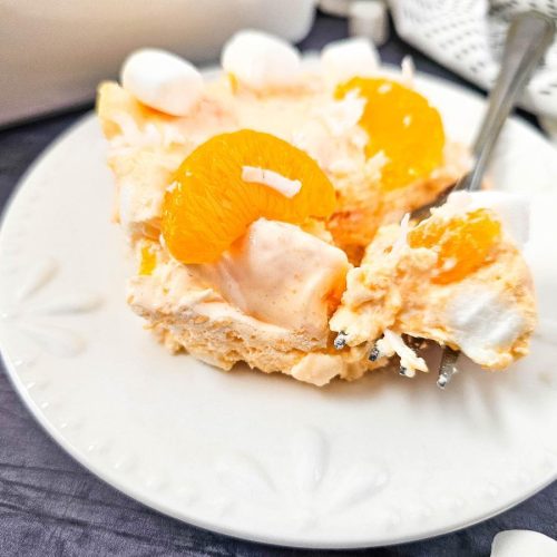 Close-up of a creamy mandarin orange jello salad with mini marshmallows and orange slices on a white plate, showing the fluffy texture and ingredients.