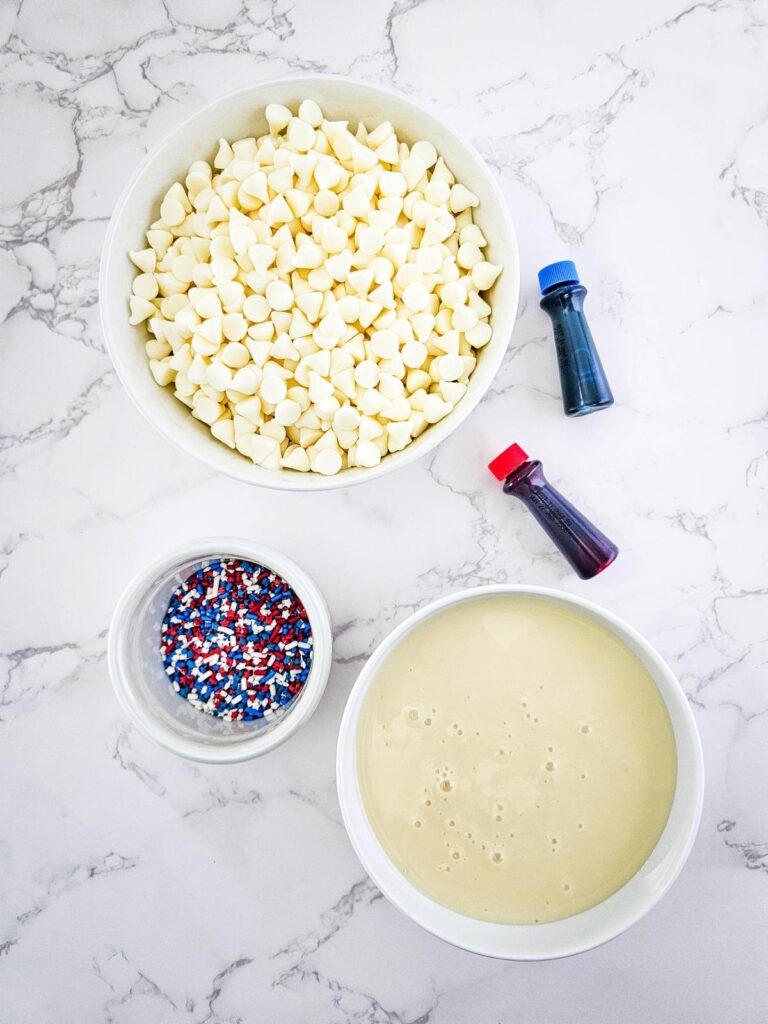 top-down view of the ingredients for 4th of july fudge, including white chocolate chips, sweetened condensed milk, food coloring, and sprinkles