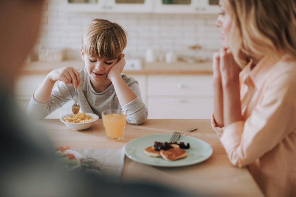 Young boy eating cereal at the breakfast table with mom in a bright kitchen during a busy school morning routine.