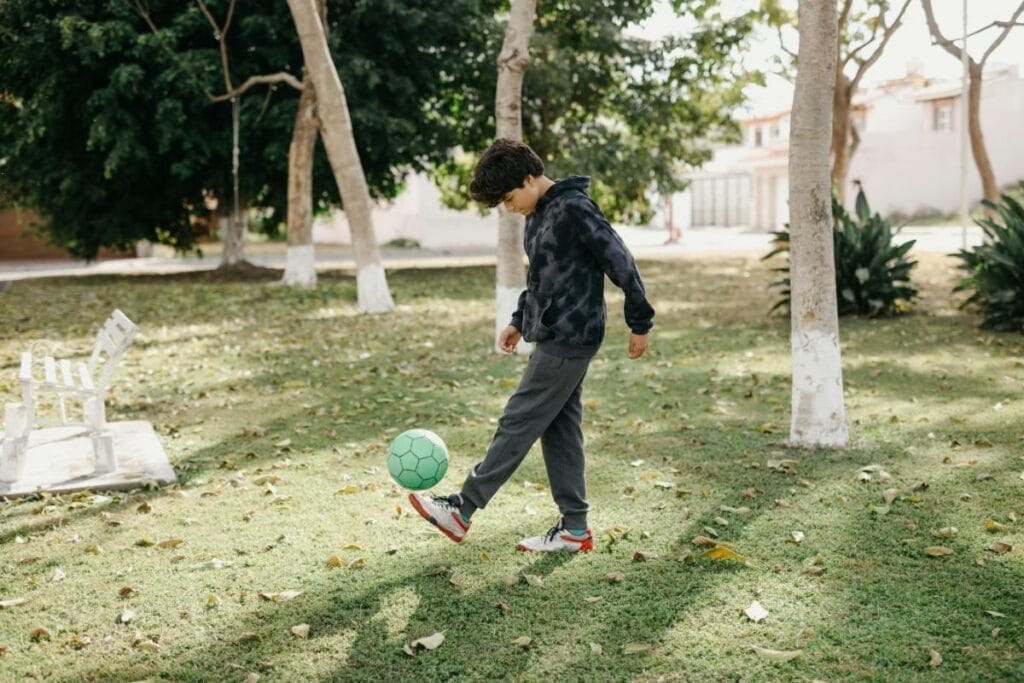 Young boy practicing soccer skills alone in a park, focusing on ball control and footwork on a sunny day