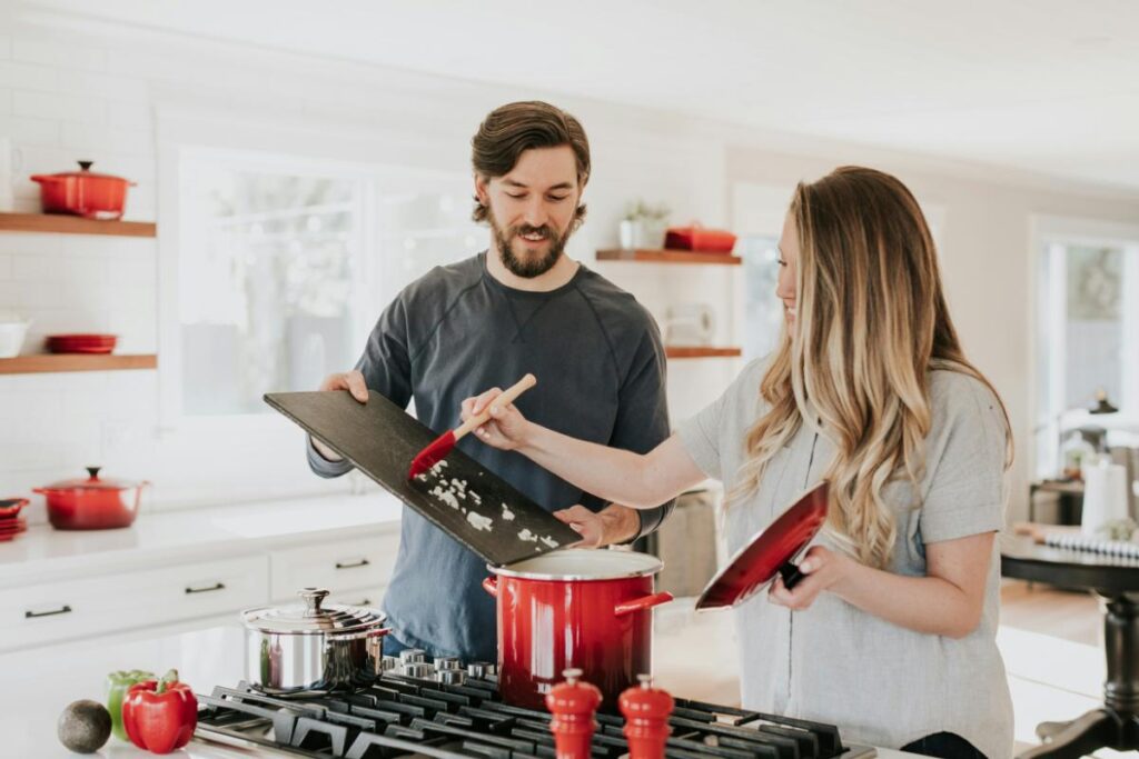 Smiling couple cooking a healthy meal together in a modern kitchen, demonstrating important adult life skills like basic cooking and meal preparation.