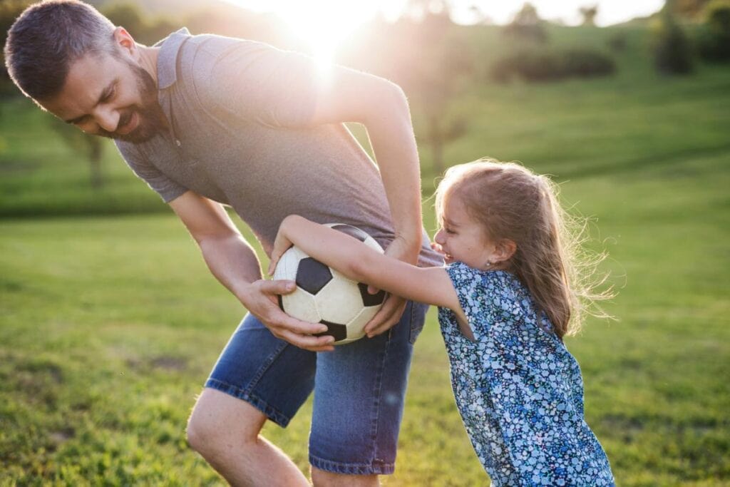 Father and daughter playfully competing for a soccer ball during outdoor family time on a grassy field