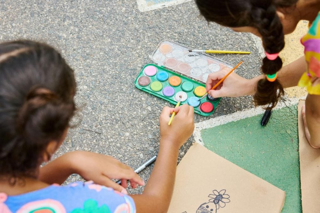 two girls painting on paper outdoors