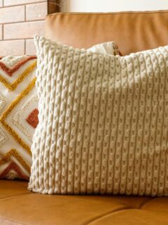 Warm caramel leather couch featuring a chunky knit cream pillow and a decorative diamond-patterned pillow in orange and yellow tones, perfect for cozy living room decor.