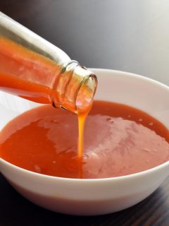 pouring hot sauce into a white bowl