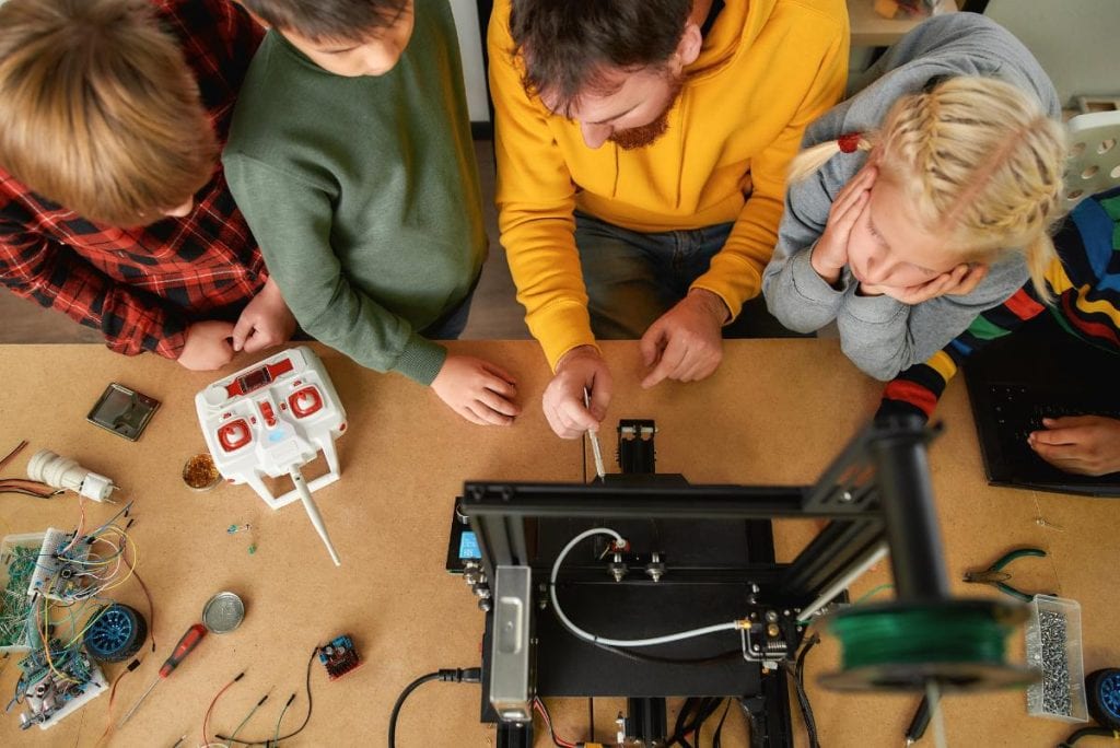 kids and teacher using a 3d printer