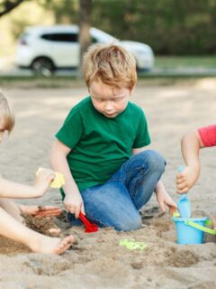 three children (2 boys and a girl) playing in the sand with shovels and a pail