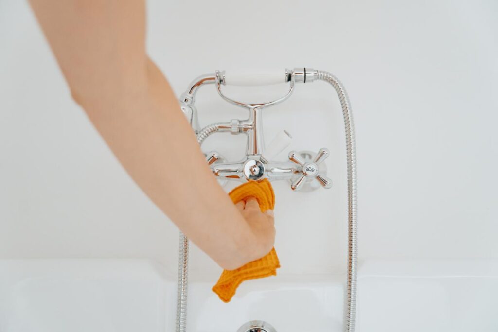 Close-up of a person cleaning and wiping down a chrome bathtub faucet as part of regular home maintenance and cleaning tasks.