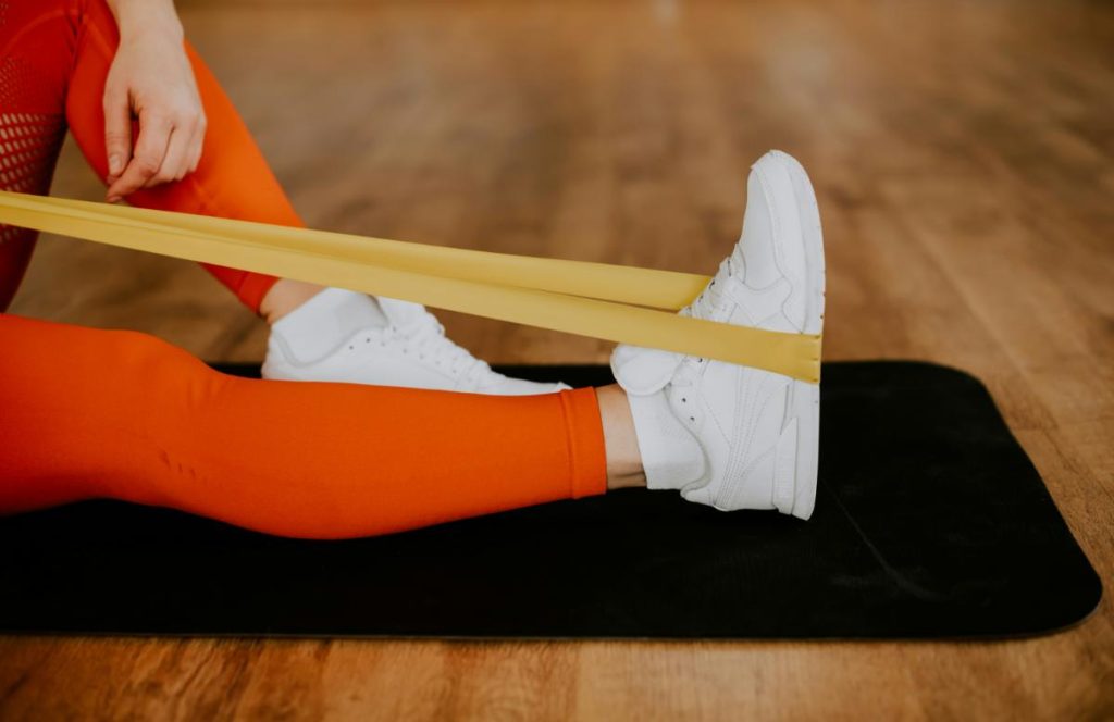 woman in orange leggings using a yellow resistance band for exercise