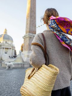 Traveler walking through Piazza del Popolo in Rome with a scarf blowing in the wind