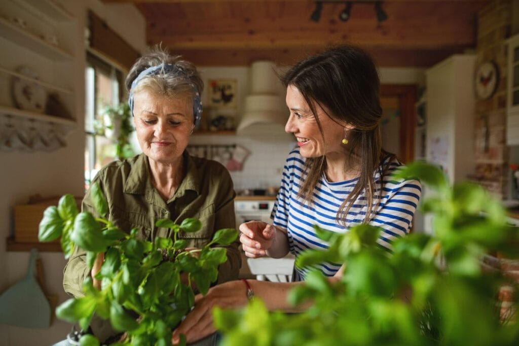 Older woman and younger woman enjoying gardening together in a bright kitchen, illustrating shared activities in a multigenerational home.