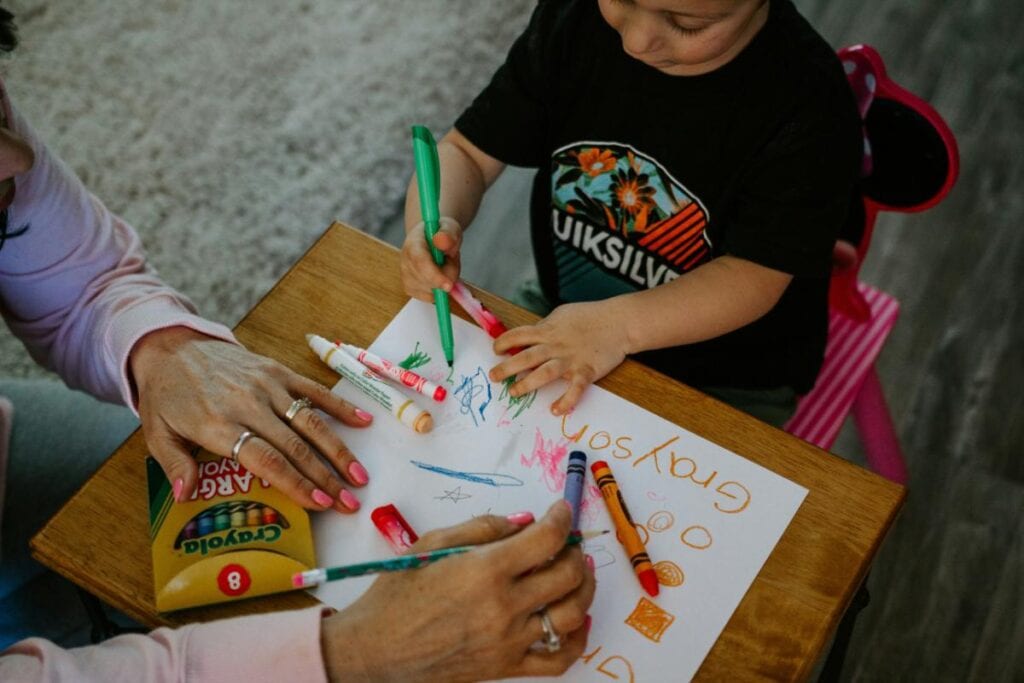 a child and mother writing and coloring on a piece of paper