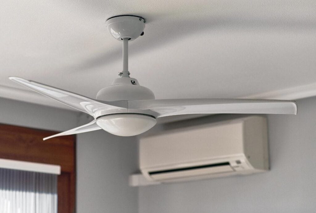 Modern white ceiling fan and wall-mounted air conditioning unit working together to keep a home cool and energy efficient during summer heat.