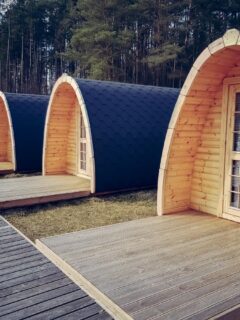 Row of modern wooden tiny house pods with curved roofs, set along a boardwalk in a forest retreat, ideal for sustainable micro living or glamping.