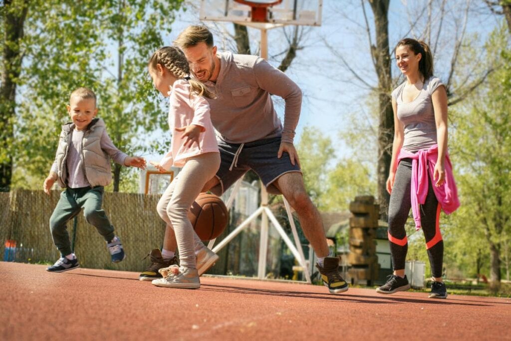 Smiling family playing basketball together outdoors, promoting active lifestyle and physical fitness as part of a healthy family routine.