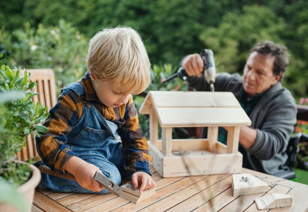 Child and grandparent building a wooden birdhouse outdoors as a fun DIY craft project for the family.