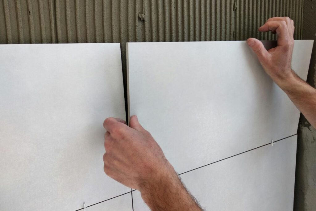 Hands positioning white ceramic wall tiles with spacers during installation, showing professional tiling techniques for kitchens and bathrooms.