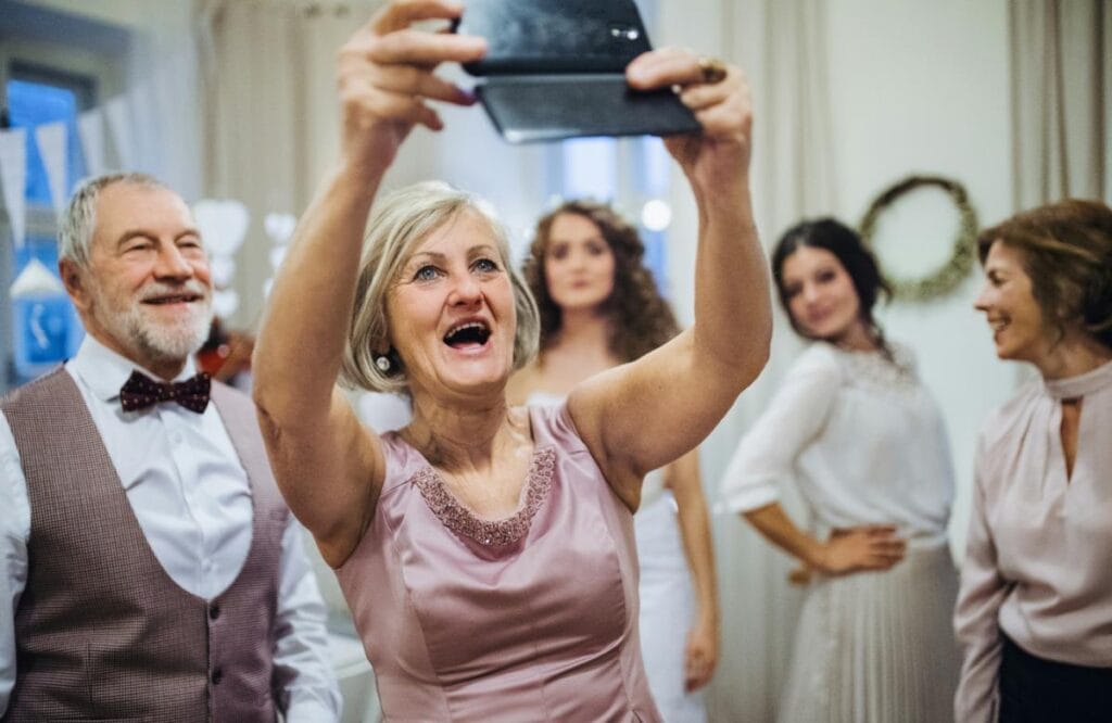 Mother of the bride in a pink dress taking a joyful selfie with wedding guests in elegant outfits, highlighting stylish mother-of-the-bride fashion ideas.