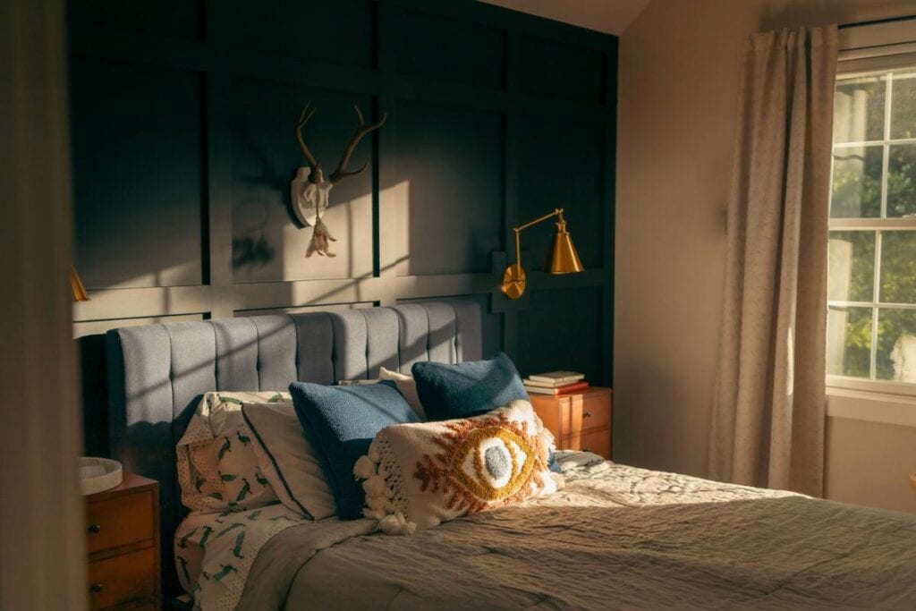 Moody bedroom with a navy blue accent wall, gold wall sconces, and layered bedding—great example of a weekend home improvement project.
