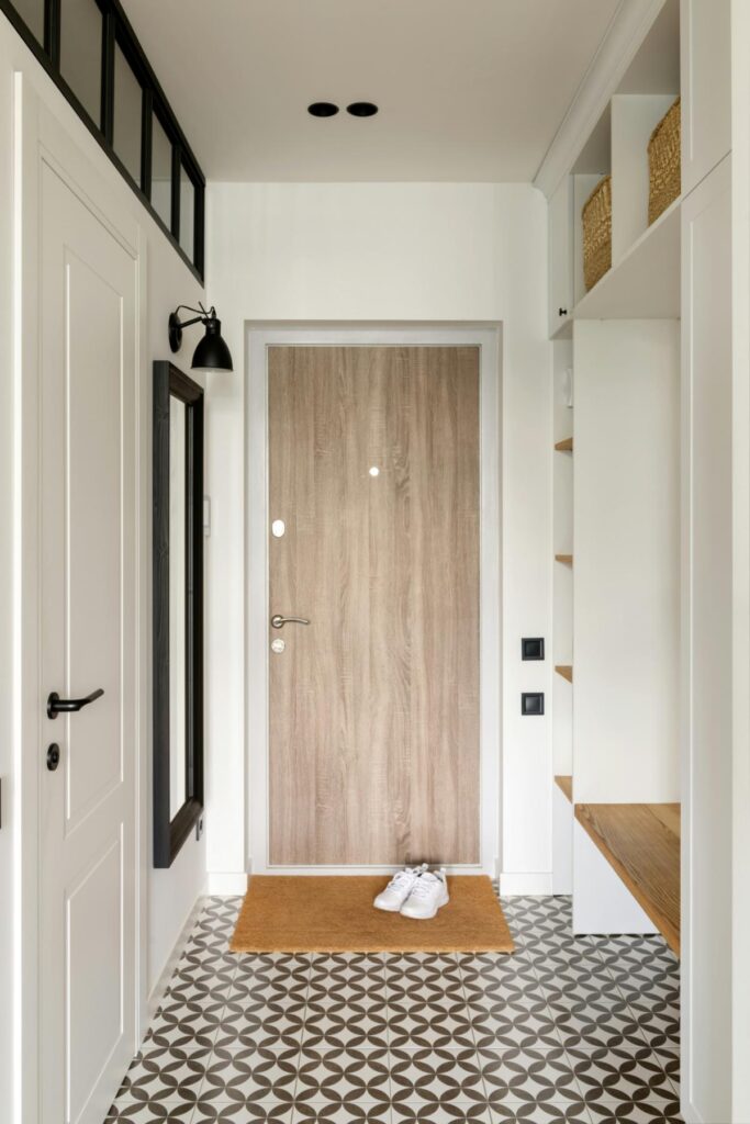 Clean, organized entryway showcasing high-traffic area maintenance, featuring patterned tile flooring, a neat doormat, white sneakers, and built-in storage solutions.