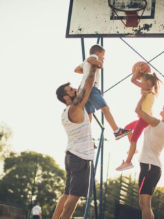 Parents helping their children shoot basketballs, encouraging physical activity, teamwork, and family fun through an active lifestyle.