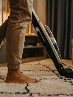 Close-up of a person vacuuming a patterned living room carpet, demonstrating effective home cleaning techniques and maintenance to prolong carpet life.