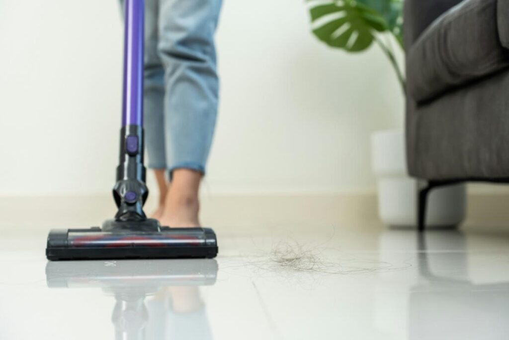 A person using a cordless vacuum cleaner on a tile floor, effectively removing dirt and pet hair.