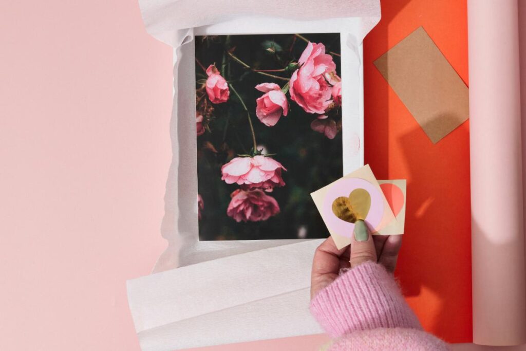 Woman adding heart-shaped stickers to custom wrapped Etsy package with floral art print and branded tissue paper