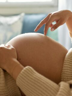 unidentified pregnant woman laying down and walking her fingers across her bare belly