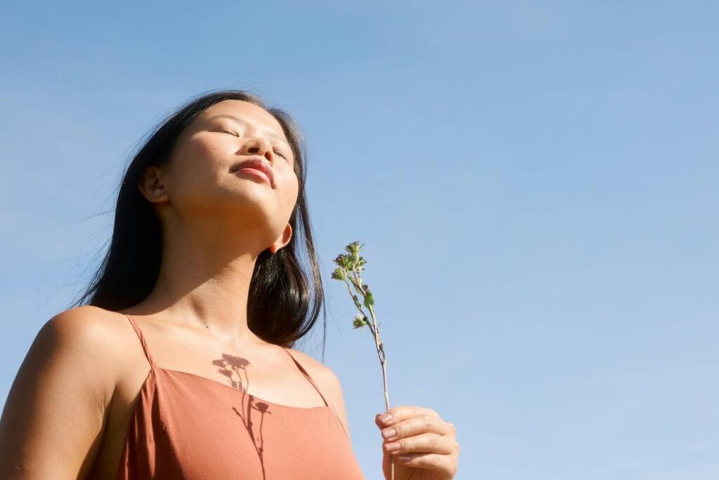 woman holding a flower and tilting her face up to the sun