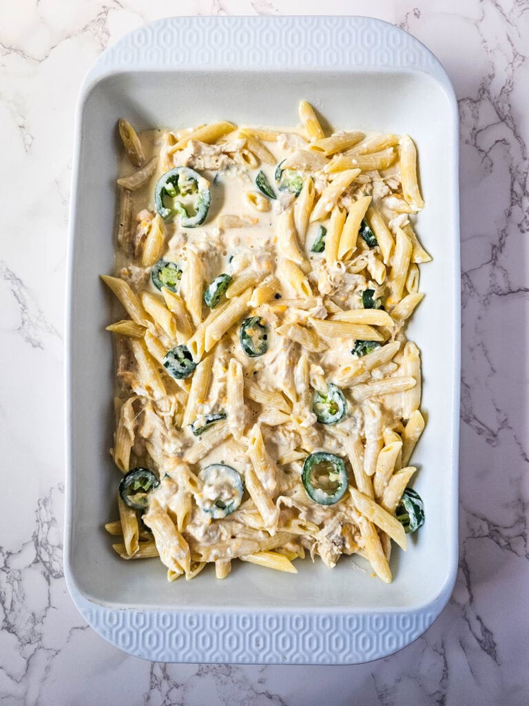 Chicken, pasta, and jalapeños spread in a 9x13 baking dish—the base layer of jalapeño popper chicken casserole.