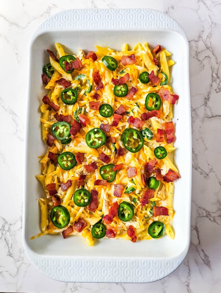 Casserole topped with crispy bacon and jalapeños, ready for the final bake.