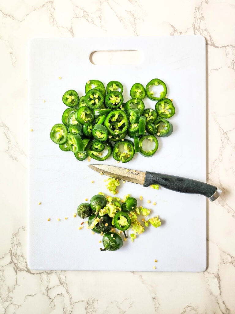Fresh jalapeños sliced and seeded on a cutting board with a paring knife.