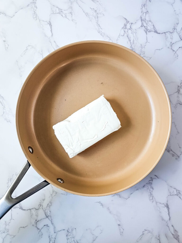 Cream cheese in a skillet to start the sauce for jalapeño popper chicken casserole.