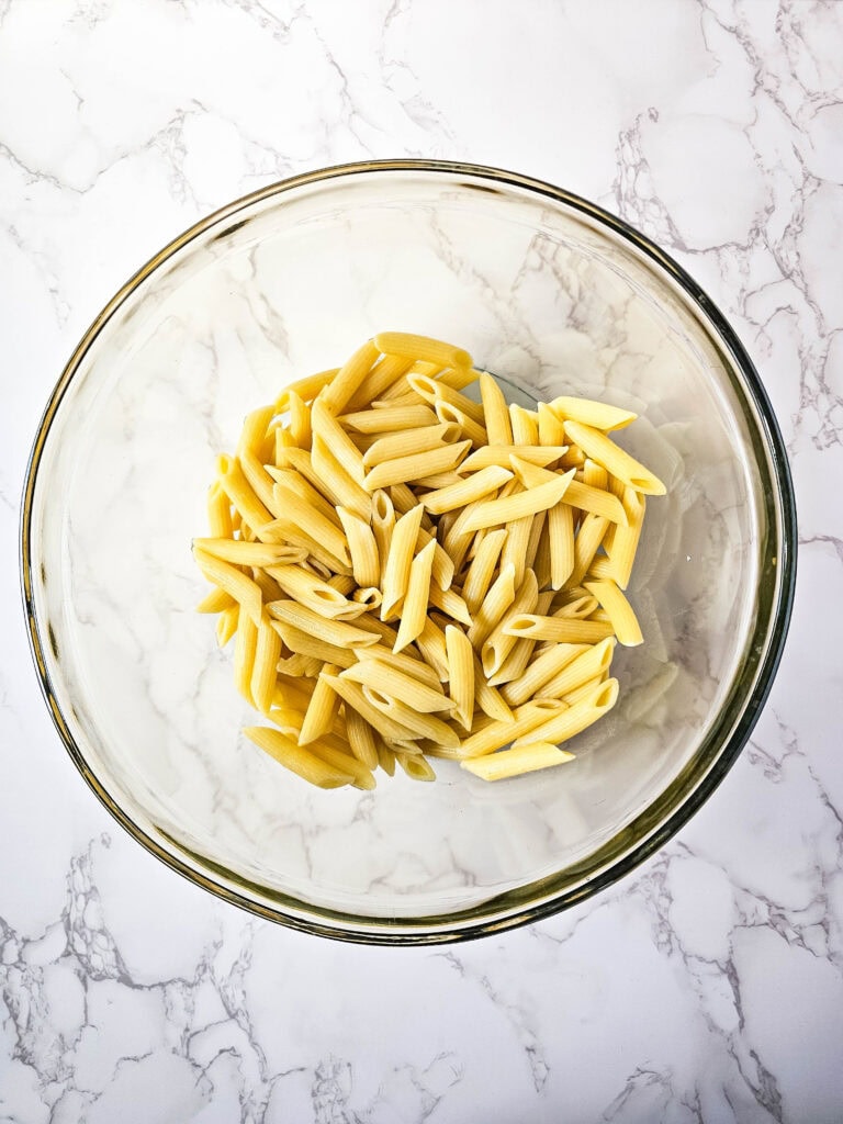 Drained cooked penne in a large glass bowl, ready to combine with sauce.
