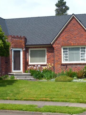 Charming brick house with gabled roof, white-trimmed windows, and lush front yard landscaping, highlighting strong and durable brick siding.
