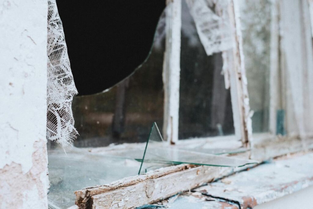 lose-up of a broken window with shattered glass and peeling paint on a deteriorating wooden sill.