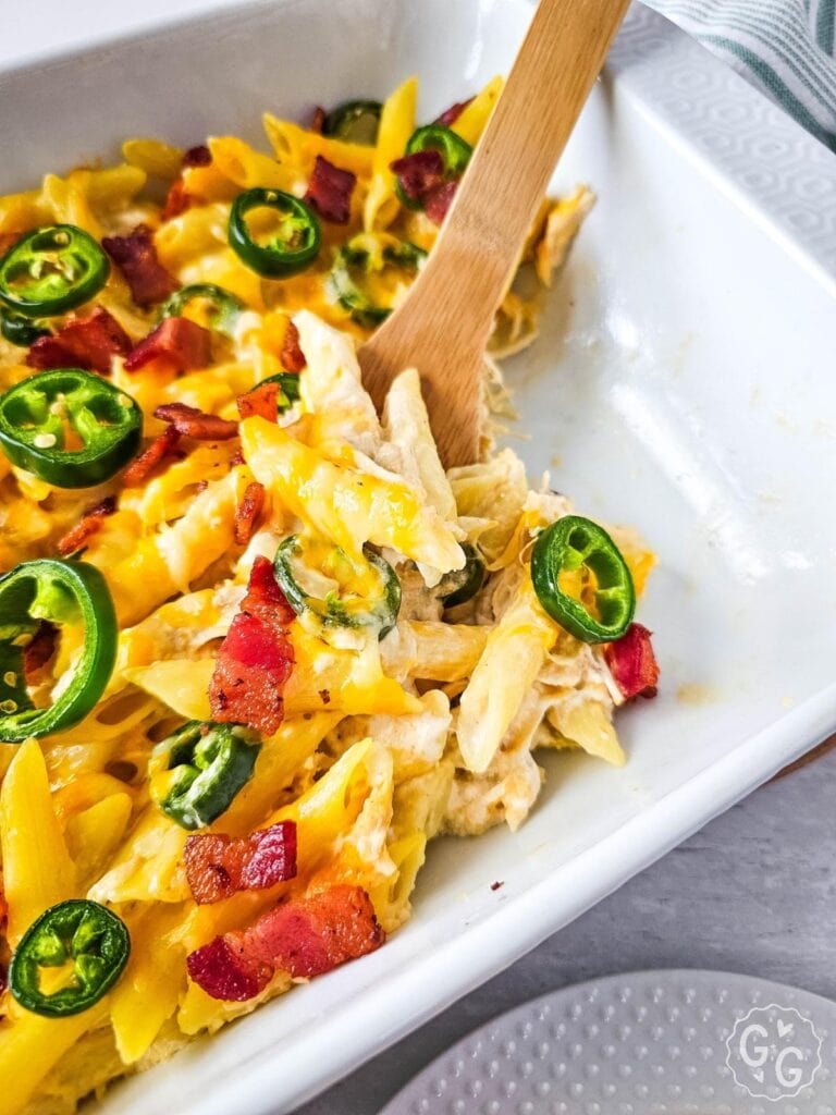 Close-up scoop of cheesy jalapeño popper chicken casserole with crispy bacon and fresh jalapeños.