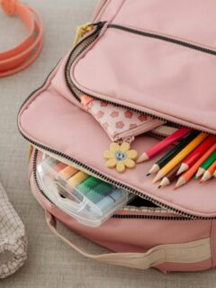 Open pink backpack filled with colorful school supplies, markers, and pencils, alongside matching shoes and headphones—perfect for back-to-school season.