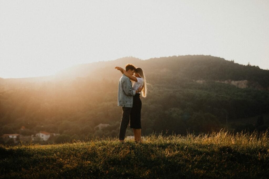 man and woman embracing on a grassy hill at sunset