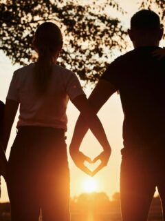 family of 4 looking at a sunset, parents making a heart shape with their hands