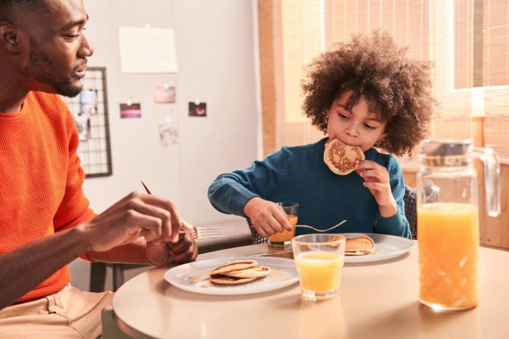 Parent and child enjoying pancakes and orange juice at breakfast, highlighting family routines and morning bonding before the school day begins.