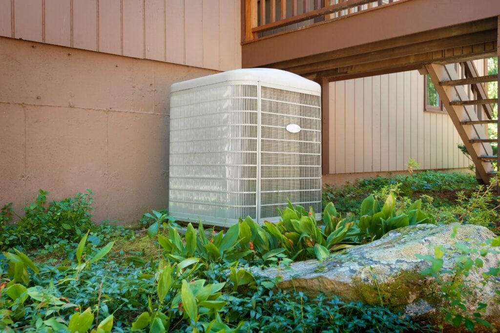 Outdoor heat pump unit installed next to a modern home with surrounding greenery, representing energy-efficient HVAC systems for eco-friendly upgrades.