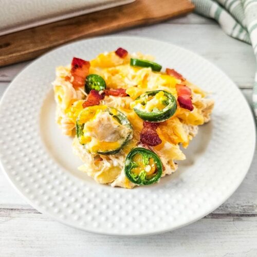 Close-up of jalapeño popper chicken casserole—melty cheese, jalapeño rounds, and crispy bacon on a white plate.