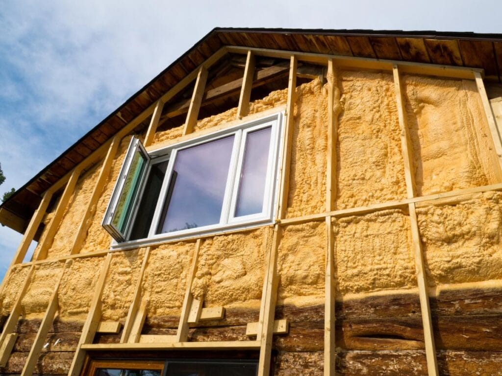 Exterior view of a home renovation with spray foam insulation applied to the walls, highlighting energy-efficient upgrades to reduce heat loss.