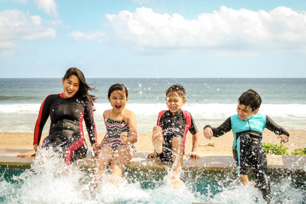 mom and kids poolside at a beach kicking their feet in the water
