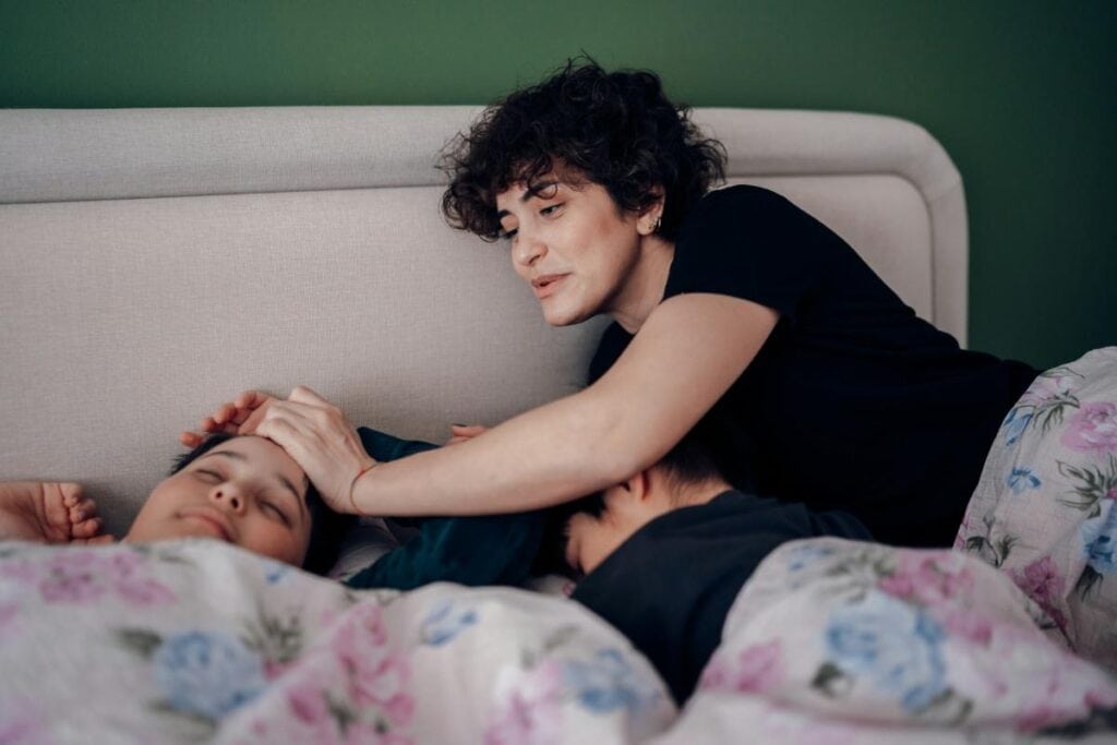 Mother gently waking her children in bed, reinforcing the importance of sleep routines and helping kids adjust to a school schedule.