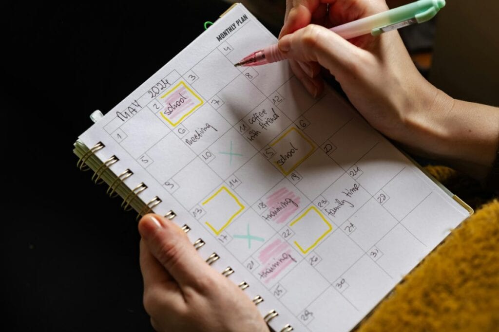 Close-up of hands holding a spiral-bound monthly calendar with highlighted school events and reminders, illustrating school year organization.
