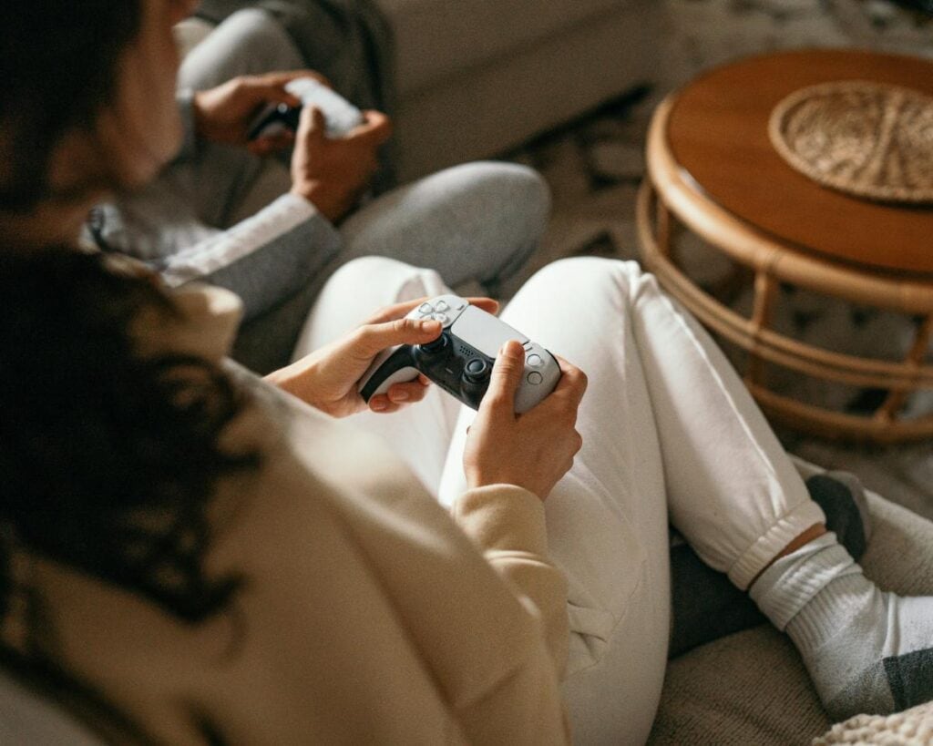 Two people holding video game controllers while sitting on a couch, illustrating relaxed screen time as part of a flexible summer routine.